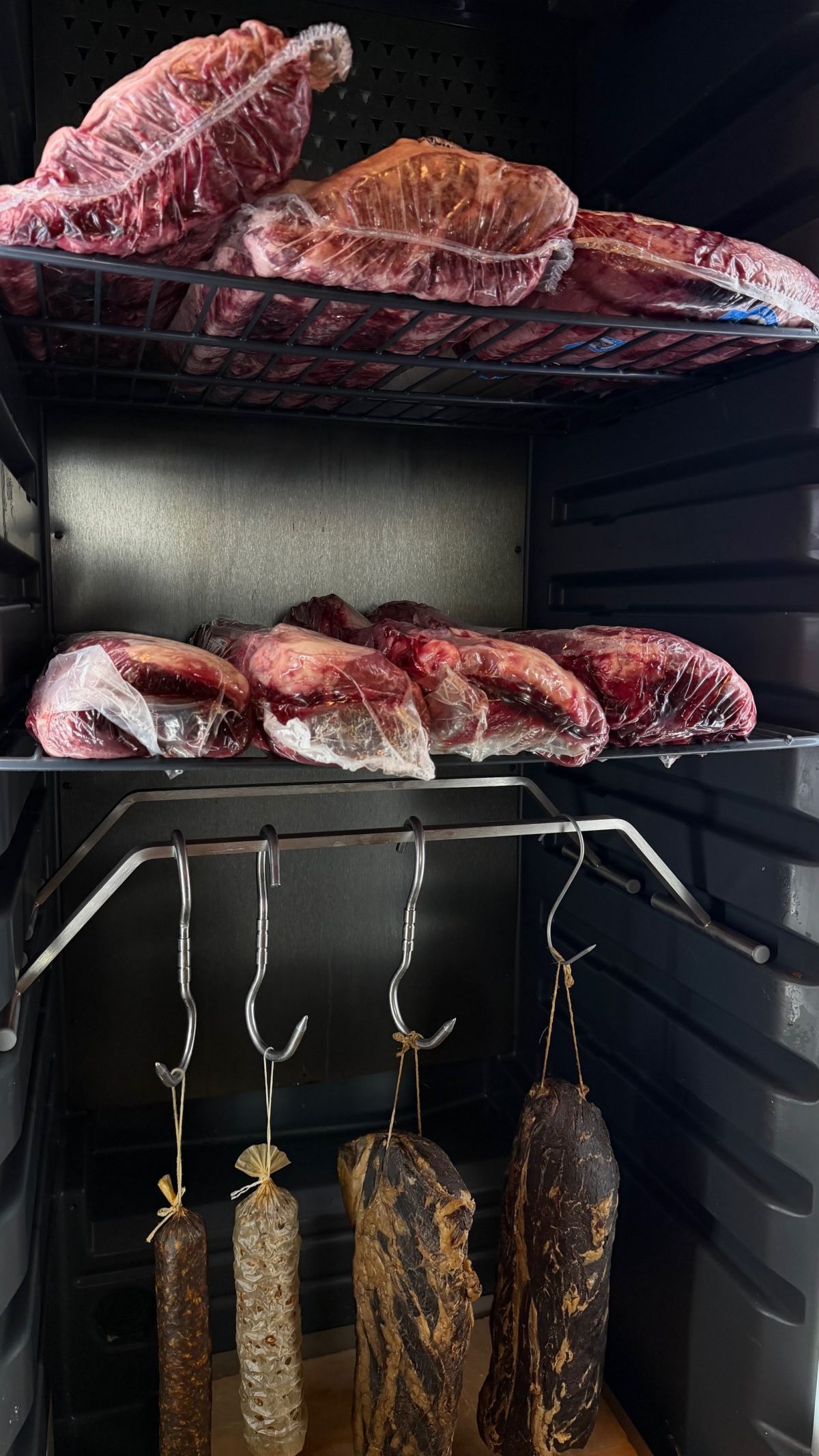 Fleisch im Reifeschrank neben luftgetrockneten Würsten